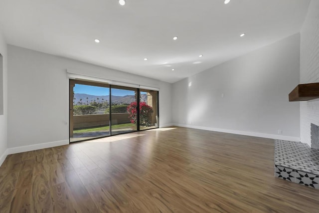 unfurnished living room featuring a mountain view, dark wood-type flooring, and a brick fireplace