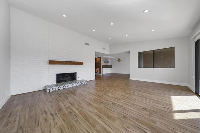 unfurnished living room featuring a brick fireplace, hardwood / wood-style flooring, and vaulted ceiling