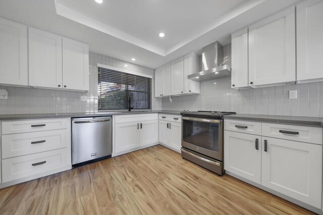 kitchen with white cabinets, decorative backsplash, wall chimney exhaust hood, and stainless steel appliances