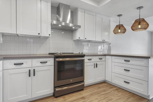 kitchen with stainless steel stove, wall chimney exhaust hood, decorative backsplash, and white cabinets