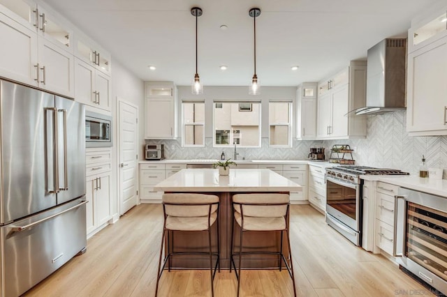 kitchen featuring wall chimney exhaust hood, white cabinetry, a kitchen island, stainless steel appliances, and beverage cooler