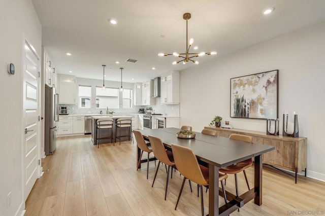 dining room featuring sink, a notable chandelier, and light hardwood / wood-style flooring