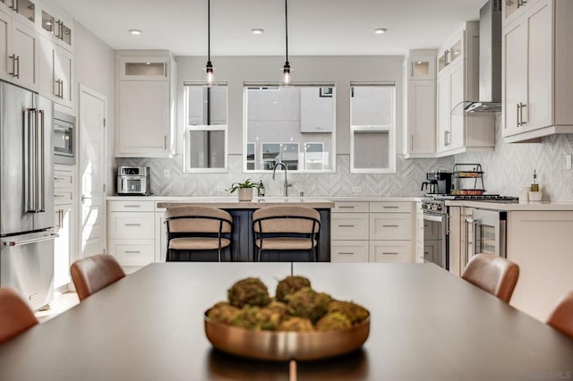 kitchen featuring appliances with stainless steel finishes, white cabinets, a kitchen breakfast bar, hanging light fixtures, and wall chimney exhaust hood