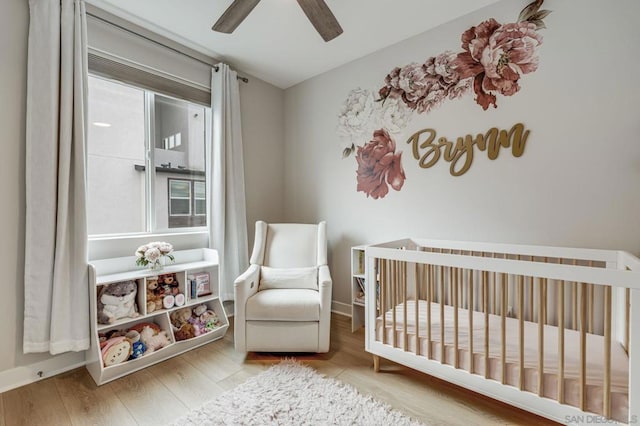 bedroom with multiple windows, light hardwood / wood-style flooring, a nursery area, and ceiling fan