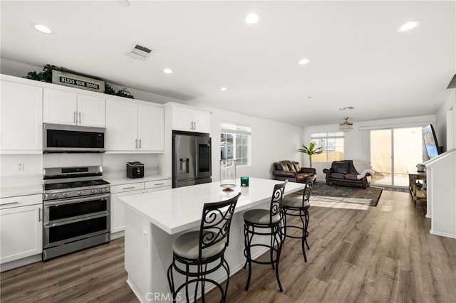 kitchen with a kitchen bar, appliances with stainless steel finishes, wood-type flooring, a center island, and white cabinetry