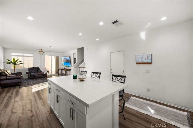 kitchen featuring dark hardwood / wood-style flooring, a kitchen island, ceiling fan, white cabinetry, and a breakfast bar area