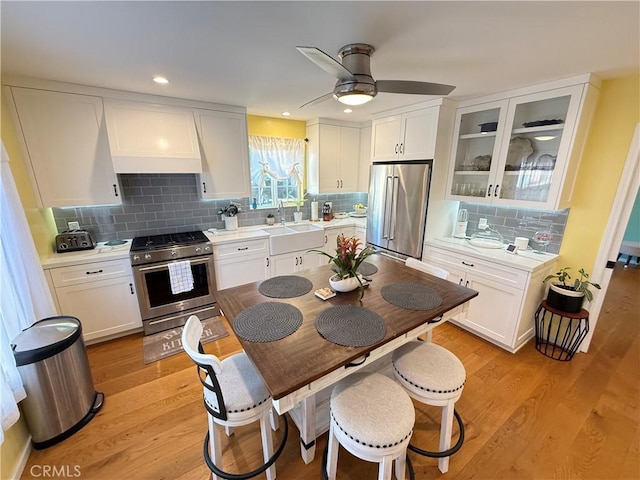 kitchen featuring light hardwood / wood-style floors, ceiling fan, stainless steel appliances, custom range hood, and white cabinets