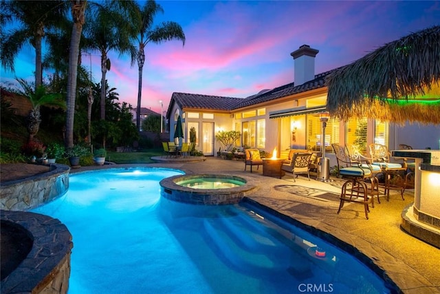 pool at dusk featuring an in ground hot tub, a patio, and a fire pit