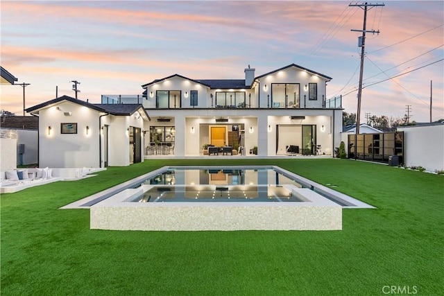 back house at dusk featuring a pool with hot tub, a lawn, a patio area, and a balcony