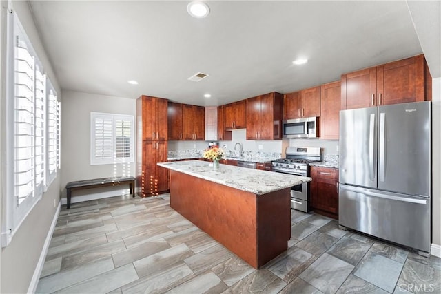 kitchen with stainless steel appliances, light stone counters, a kitchen island, and sink