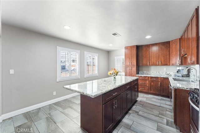 kitchen with light stone countertops, sink, stainless steel stove, and a center island