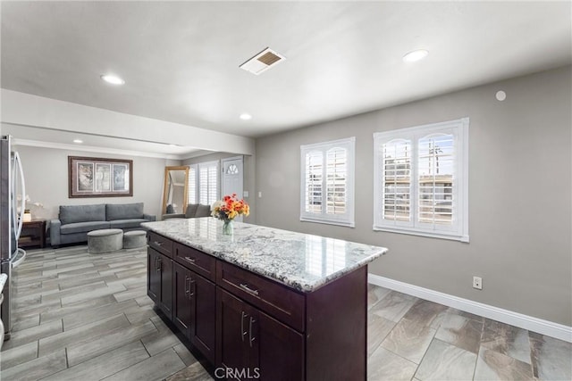 kitchen featuring stainless steel fridge, dark brown cabinets, light stone counters, and a center island