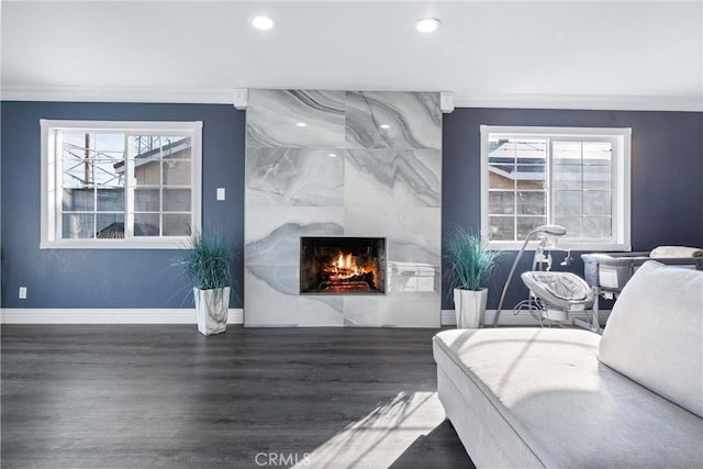 living room with dark wood-type flooring, a fireplace, a wealth of natural light, and crown molding