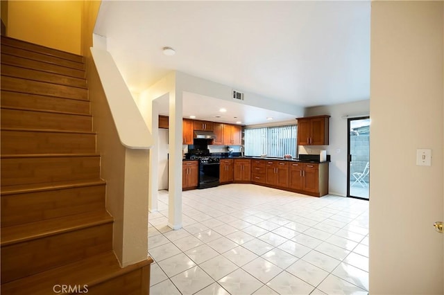 kitchen featuring black gas range oven, light tile patterned floors, and stainless steel refrigerator