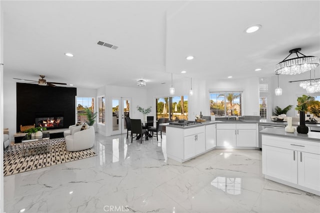 kitchen with ceiling fan, a fireplace, pendant lighting, kitchen peninsula, and white cabinetry