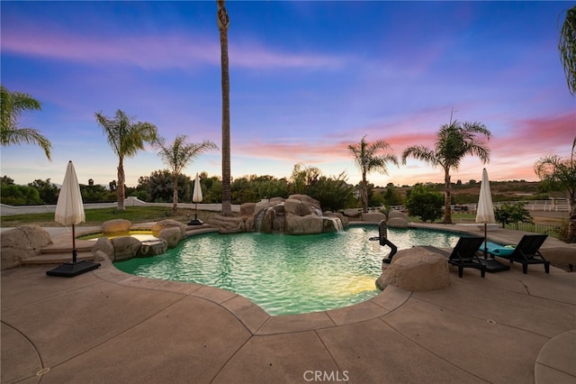 pool at dusk with a patio area and pool water feature