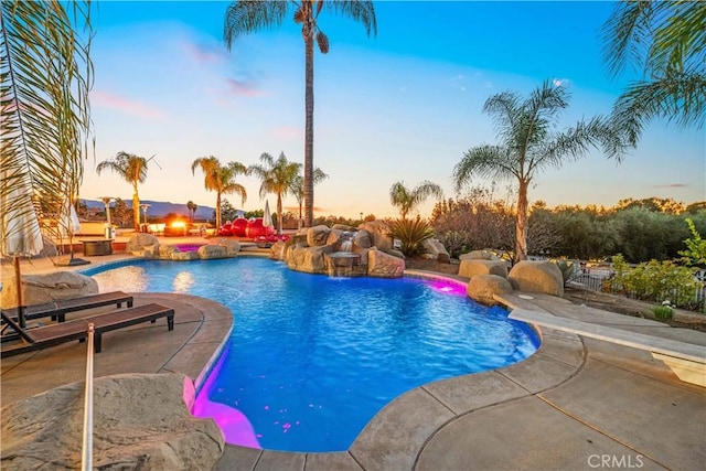 pool at dusk featuring pool water feature and a patio