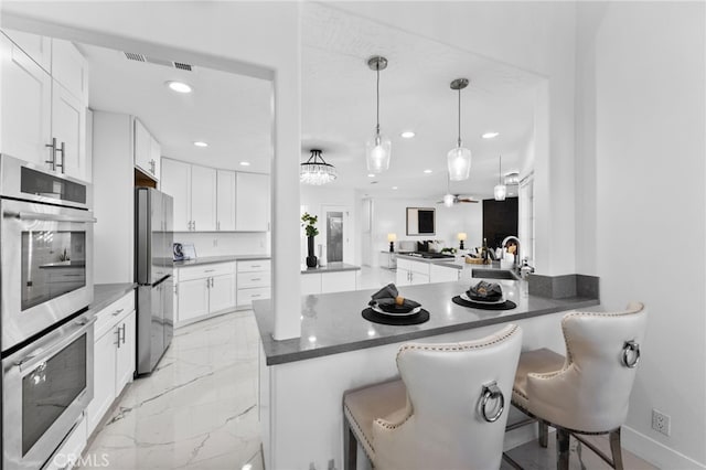 kitchen with a kitchen bar, kitchen peninsula, stainless steel appliances, white cabinets, and sink