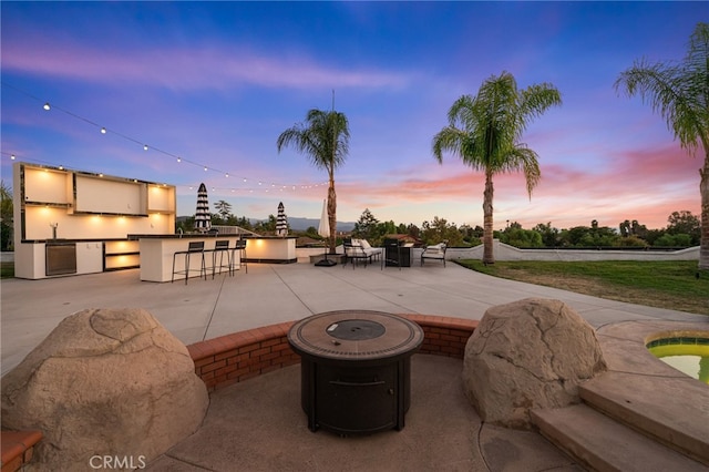 patio terrace at dusk with an outdoor bar, a fire pit, and area for grilling