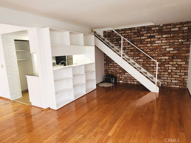 unfurnished living room with hardwood / wood-style flooring and brick wall