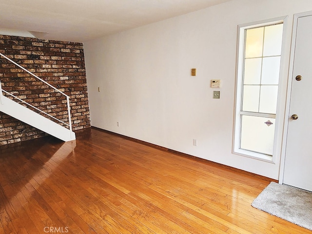 unfurnished living room featuring hardwood / wood-style flooring and brick wall