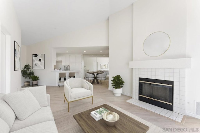 living room with lofted ceiling, a tile fireplace, and light hardwood / wood-style floors