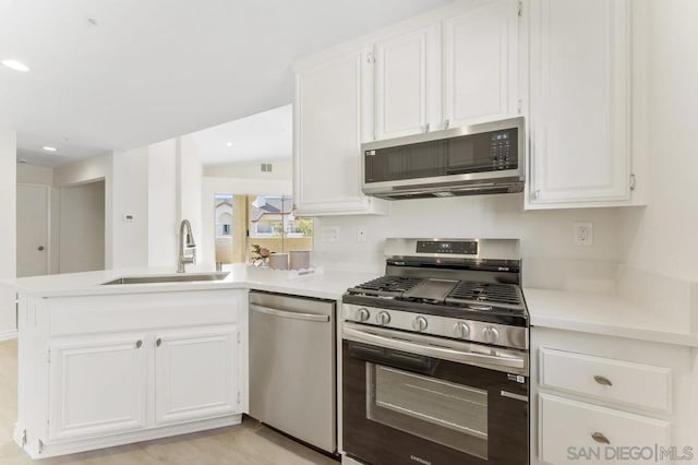 kitchen with kitchen peninsula, sink, stainless steel appliances, and white cabinetry