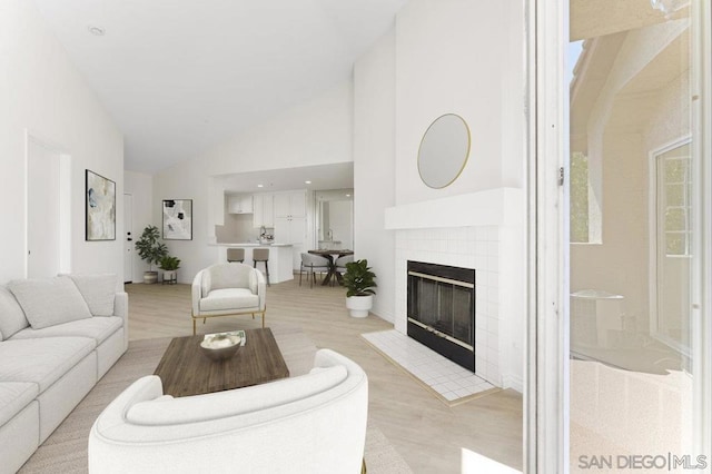 living room with high vaulted ceiling, a tile fireplace, and light hardwood / wood-style flooring