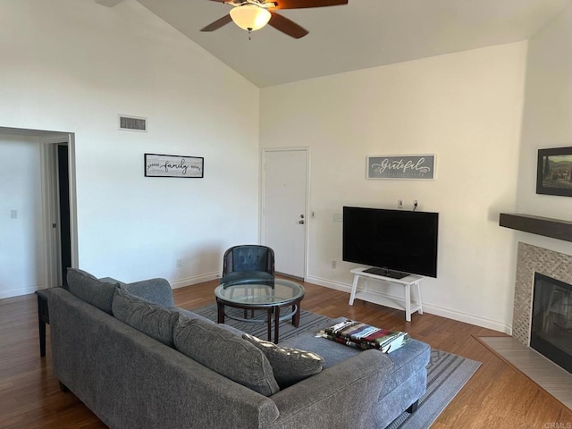 living room with ceiling fan, wood-type flooring, high vaulted ceiling, and a tiled fireplace