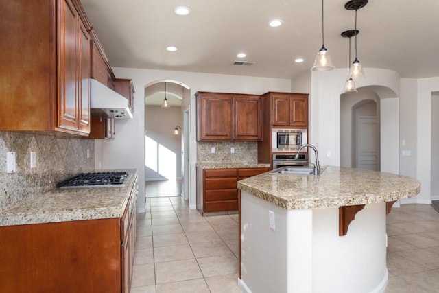 kitchen with tasteful backsplash, an island with sink, hanging light fixtures, and exhaust hood