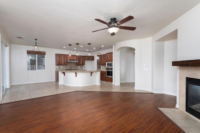 unfurnished living room featuring a tiled fireplace, light hardwood / wood-style floors, and ceiling fan