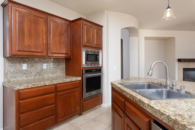 kitchen with sink, a tile fireplace, appliances with stainless steel finishes, backsplash, and light tile patterned flooring