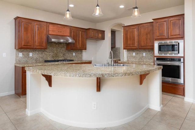 kitchen featuring sink, appliances with stainless steel finishes, range hood, a kitchen breakfast bar, and decorative light fixtures