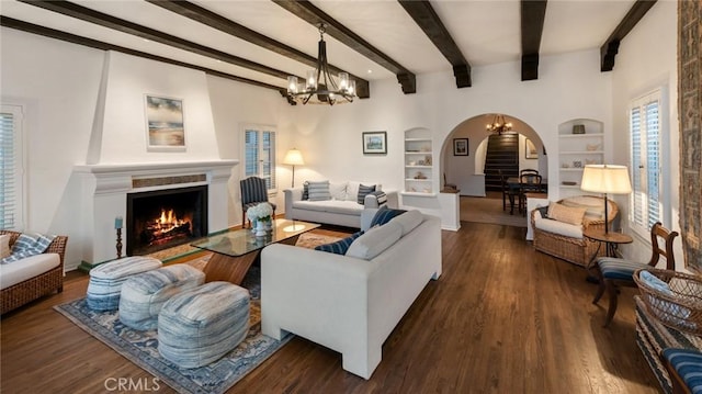 living room featuring built in shelves, a large fireplace, dark hardwood / wood-style flooring, and a chandelier