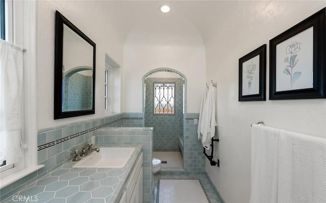 bathroom featuring tile patterned flooring, vanity, a shower, tile walls, and toilet