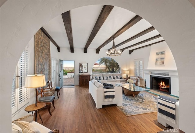 living room with hardwood / wood-style flooring, a notable chandelier, heating unit, a fireplace, and beam ceiling