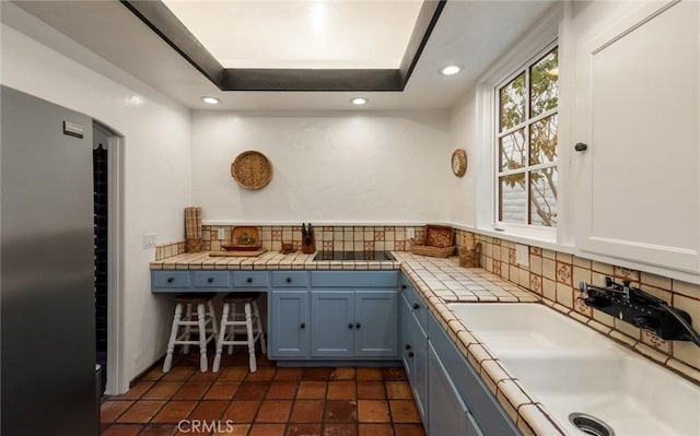 kitchen with decorative backsplash, sink, blue cabinetry, tile countertops, and a tray ceiling