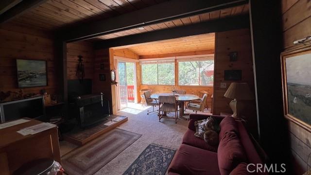 carpeted living room featuring wood ceiling, a wood stove, wood walls, and lofted ceiling with beams