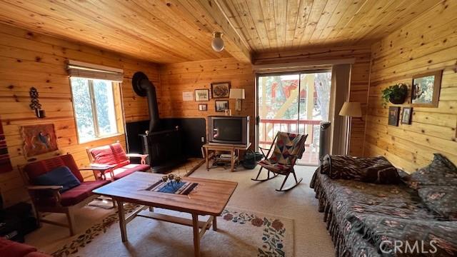 carpeted living room with a wealth of natural light, wooden walls, a wood stove, and wooden ceiling