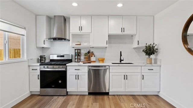 kitchen featuring appliances with stainless steel finishes, white cabinets, wall chimney exhaust hood, light hardwood / wood-style flooring, and sink