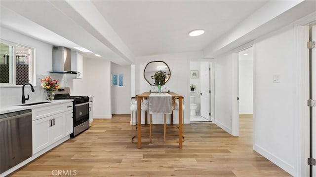 kitchen with white cabinets, appliances with stainless steel finishes, wall chimney exhaust hood, light hardwood / wood-style floors, and sink