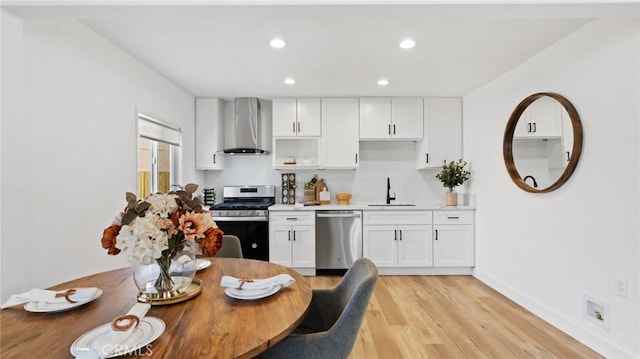 kitchen with sink, light wood-type flooring, appliances with stainless steel finishes, white cabinets, and wall chimney exhaust hood