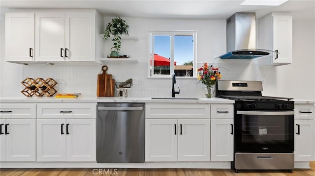 kitchen featuring stainless steel appliances, tasteful backsplash, wall chimney range hood, white cabinets, and sink