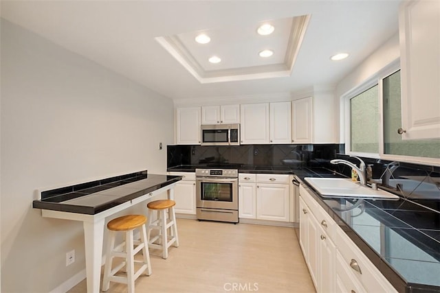 kitchen featuring stainless steel appliances, a raised ceiling, a kitchen bar, and white cabinets