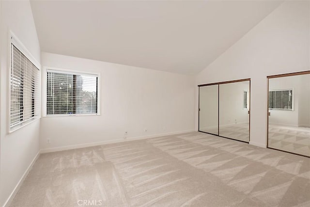 unfurnished bedroom featuring high vaulted ceiling, light colored carpet, and multiple closets