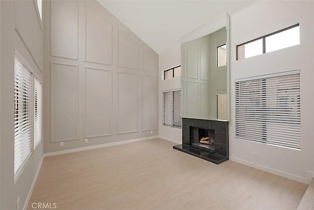 unfurnished living room with light wood-type flooring, plenty of natural light, a tile fireplace, and a towering ceiling