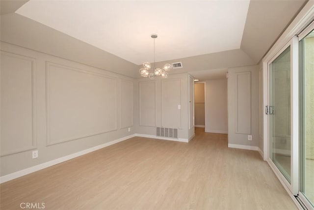 spare room with vaulted ceiling, an inviting chandelier, and light hardwood / wood-style flooring