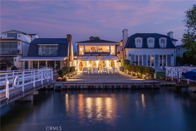 back house at dusk featuring a balcony, a patio area, and a water view