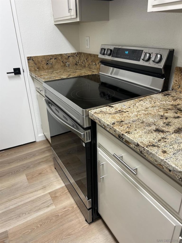 kitchen with light hardwood / wood-style floors, light stone countertops, electric range, and white cabinets