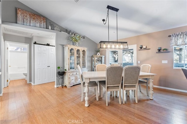 dining space with vaulted ceiling, light hardwood / wood-style floors, a barn door, and plenty of natural light